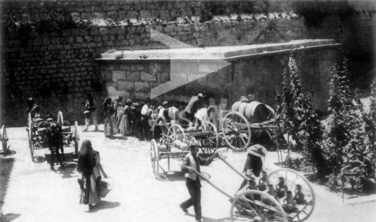 Aguaderos y aguaderas cargando agua en la fuente de la ciudad.