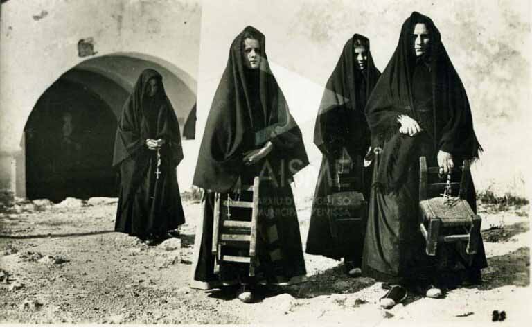 Mujeres vestidas de luto saliendo de misa con el rosario y la silla